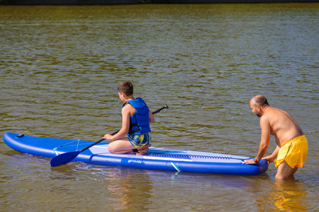 A family day at the beach: a father instructs his son in the art of stand-up paddleboarding.の写真素材