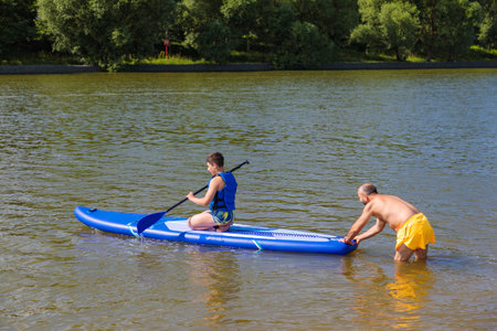 A family day at the beach: a father instructs his son in the art of stand-up paddleboarding.の写真素材