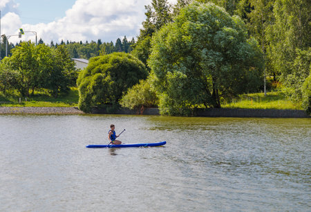 A young guy sitting down rides a SUP board, overcoming the waves with easeの写真素材