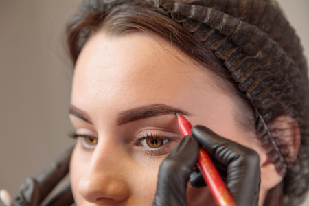 Beautician using eyebrow pencil shaping eyebrows of client in beauty salonの写真素材