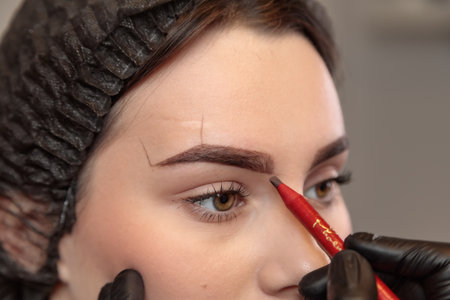 Beautician applying eyebrow makeup to young woman in beauty salon