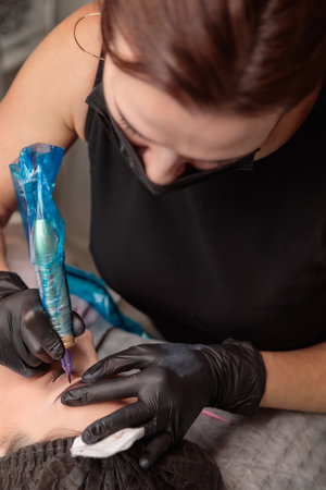 Cosmetologist applying permanent makeup on eyebrows with tattoo machineの写真素材