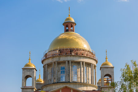 Golden domes shining on a church under construction with scaffolding and blue skyの写真素材