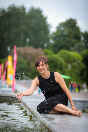 Smiling lady happily splashes water towards the camera from a cozy summer parkの写真素材
