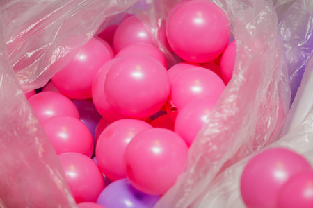 Vibrant pink plastic balls are overflowing from a clear plastic bag, creating a playful and colorful sceneの写真素材
