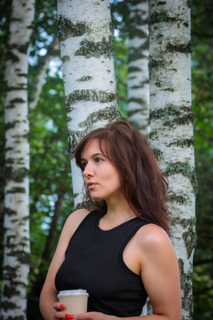 Picture of a beautiful girl with a cup of coffee among birches