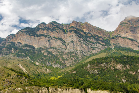 Scenic landscape showcasing the beauty of nature with towering peaks, verdant valleys, and a dramatic cloudy skyの写真素材