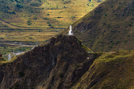 White statue standing on rocky mountain peak overlooking winding road and vast landscape in papallacta, ecuadorの写真素材