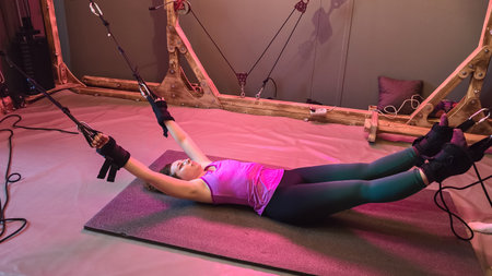 Young woman performing stretching exercises with suspension straps in gymの写真素材