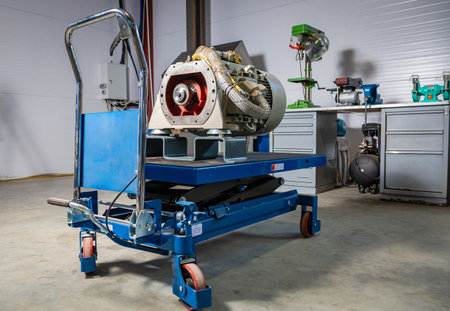 Industrial pump placed on blue hydraulic scissor lift cart with workbench and tools in background in mechanical workshopの写真素材