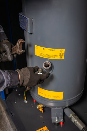 Close up of technician's hands wearing gloves, using wrench and replacing part on industrial air compressor tankの写真素材