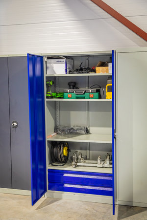 Opened metal storage cabinet holding various power tools, equipment, and supplies in an organized workshop or garageの写真素材