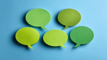 Overhead view of five blank paper speech bubbles arranged on a bright blue surface, perfect for showcasing ideas and enhancing visual storytellingの素材
