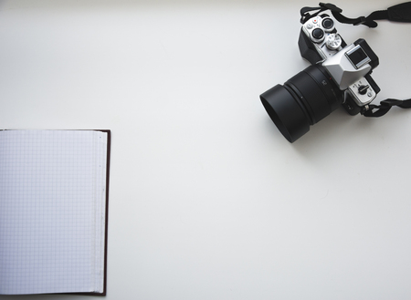 Photo camera and opened notepad on the white background top view. Flat lay