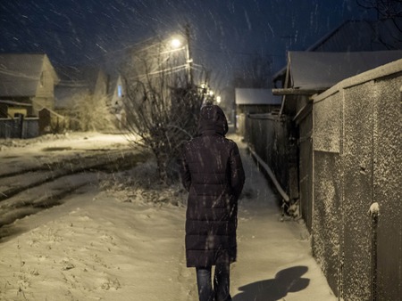 Woman walking along the street in winter evening during snowfallの写真素材