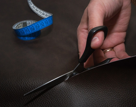 Cutting-out of brown leather in the atelier. Using blue twisted tape measure and black scissors