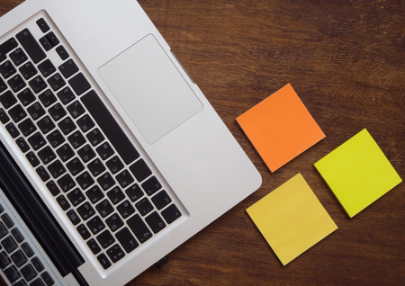 Keyboard and empty colorful stickers for notes on the wooden desk. Flat lay