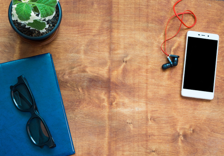 Notebook, cellphone, headphones and black glasses on wooden desk. Black blank space on the phone screen.Top view with copy space.の写真素材
