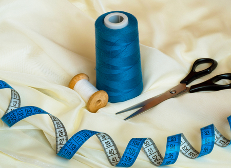 Black scissors, threads and tape measure on beige textile, macro shot, sewing concept