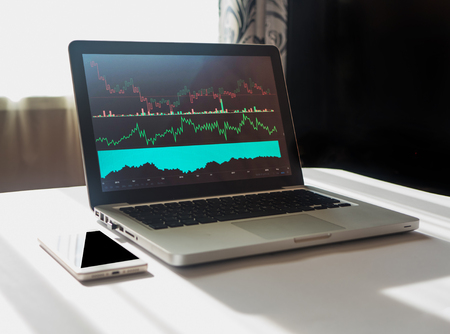 Laptop with chart on display at workplace of economist 12. Analyzing investment charts and graphs on laptop. Smartphone with black screen. Copyspaceの写真素材