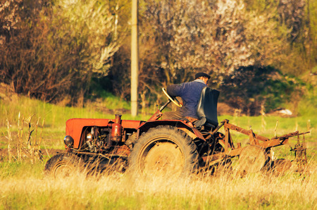 A tractor driver plowing soil in autumn to sow winter wheat. Side view of a tractor driver on tractor plowing the fieldの写真素材