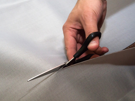 Man's hand cutting textile with tailor's scissors. Concept of fabric cutting-out. Close-up