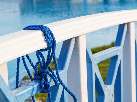Blue twisted rope tied on the wooden bridge railing with water background, closeupの写真素材