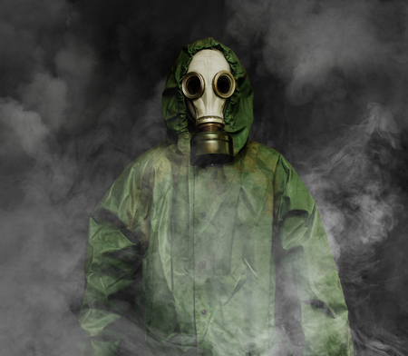 Man in gas mask and USSR cloak of chemical protection surrounded by smoke on dark backgroundの写真素材