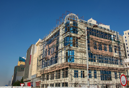 Building under construction is encased in scaffolding in Doha under blue skyの写真素材