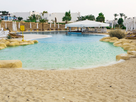 Swimming pool with sand entrance in Egypt. Empty sun-loungers near the pool at the dawnの写真素材