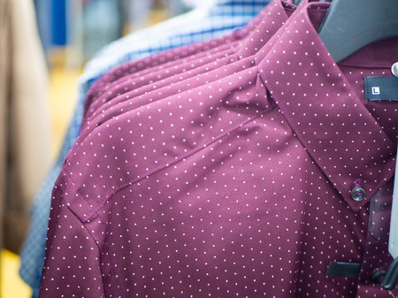 Closeup of a row of burgundy man shirts on hangers in a store or showroomの写真素材