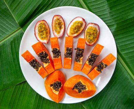 Top view of papaya slices and passion fruit on plate, green banana leaves on background, flat lay. Exotic tropical fruits.の写真素材