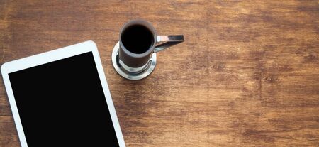 White digital tablet on a wooden table with a cup of coffee. Copy space, flat lay. Banner