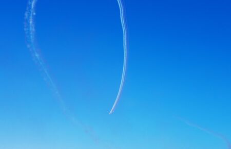 Airplanes leave curved trace on clear blue sky. View from below on the trail from many planes