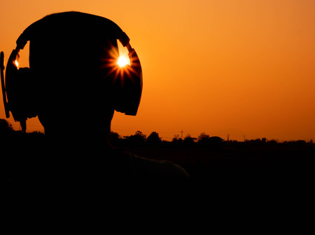 Silhouettes of teenage boys listen to music from headphones at sunset evening sky background.の写真素材