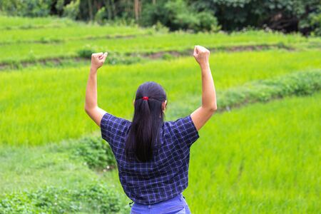 Rear of Asian young woman stand and raising her arms with a look of success on nature background.の写真素材