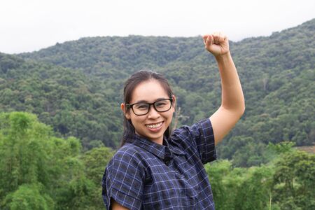 Asian young woman smile and raising her arms with a look of success on nature background.の写真素材