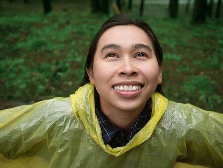 Portrait of Happy Asian woman wearing yellow raincoat stand in rain.の写真素材
