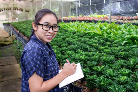 Portrait of a farmer Asian woman at work in greenhouse with notebook examines the growing seedlings on the farm and diseases in greenhouse.の写真素材