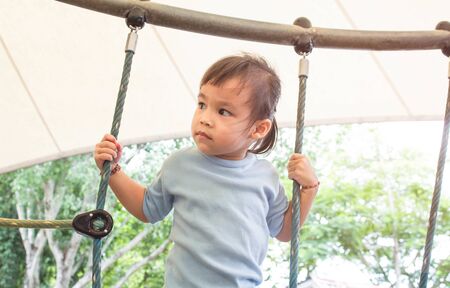 Asian little child girl having fun to climbing rope at playground in summer time.の写真素材