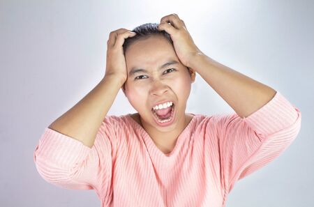 Portrait of a stressed woman holding head in hands and yells loudly angry.の写真素材