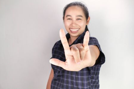 Portrait of Asian young woman in blue shirt, Showing I LOVE YOU with body language and smiley face isolated on grey background. Concept of love and concern.の写真素材