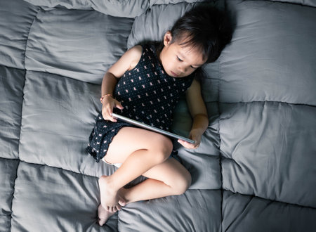 Asian little girl watching laptop on their bed. Kid addicted to mobile phones.の写真素材
