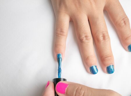 Close-up of female hands painting blue nail varnish, self made manicure at home.の写真素材