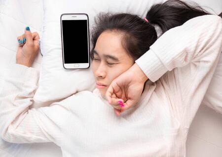 Asian young woman is sleepy while alarm clock on bed in the morning.