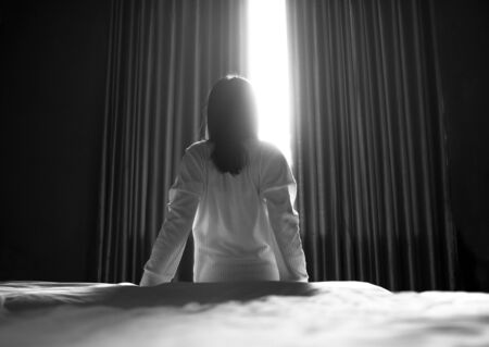 Rear of an Asian woman sitting and stretch lazily in the bright morning in bedroom. Health care concept.の写真素材
