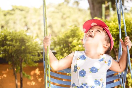 Asian little child girl having fun to play with swings in playground.