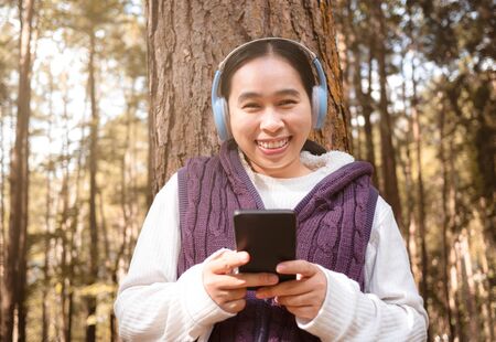 Asian young woman listening to music by headphone in the garden. Technology and relaxation concept.の写真素材