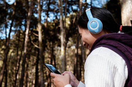 Asian young girl listening to music by headphone in the garden. Technology and relaxation concept.の写真素材