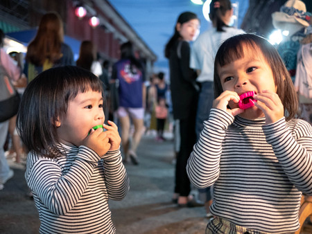 Lampang, Thailand; 5 October 2019 - Adorable Asian child girl with her sister having fun with Dracula teeth plastic toys in Kad Kong Ta Walking Street.のeditorial素材